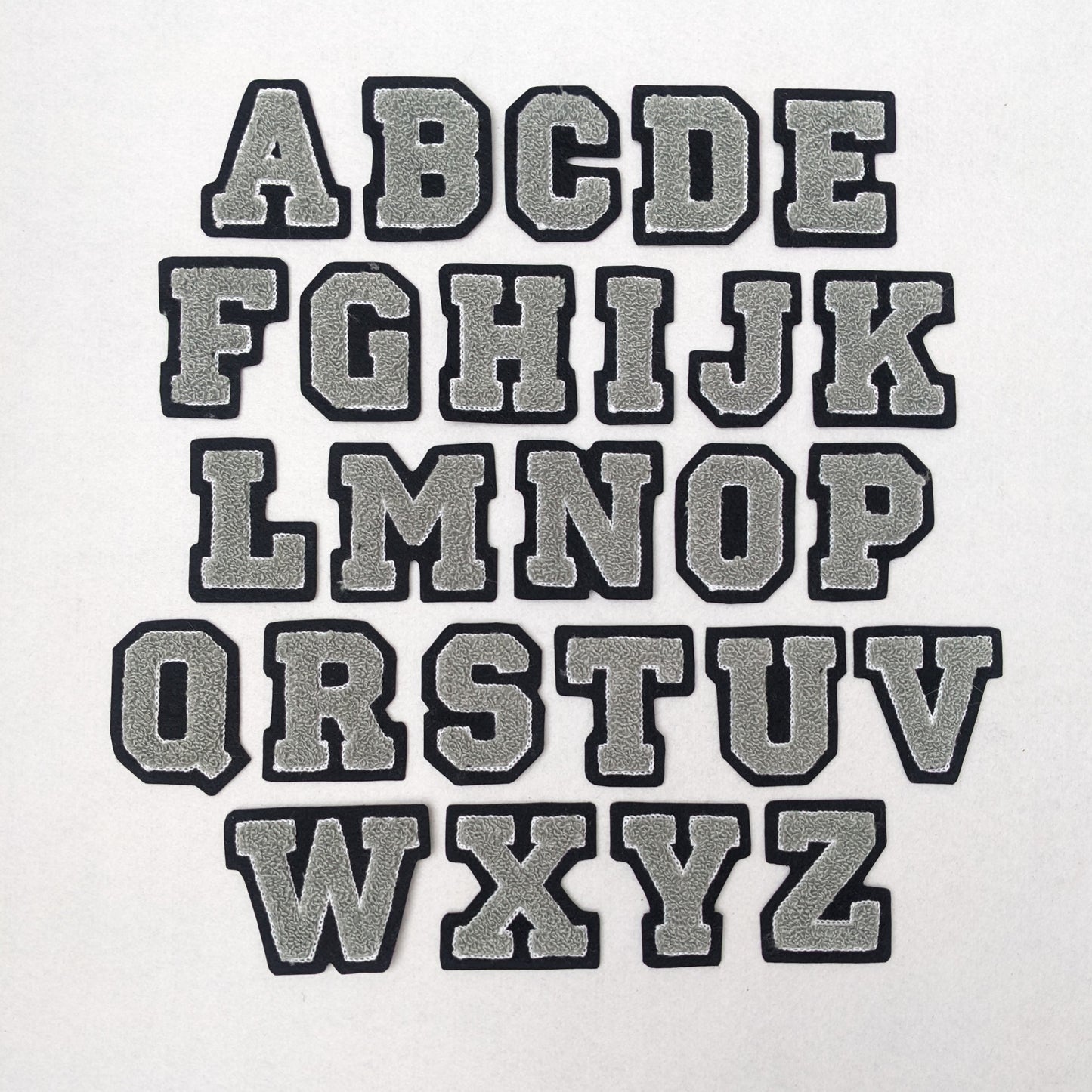 Grey chenille block letter with white outline on black colored felt.