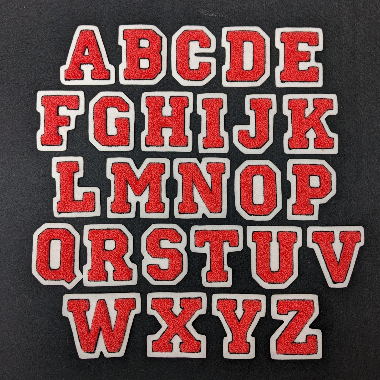 Coral chenille block letter with black outline on white colored felt.