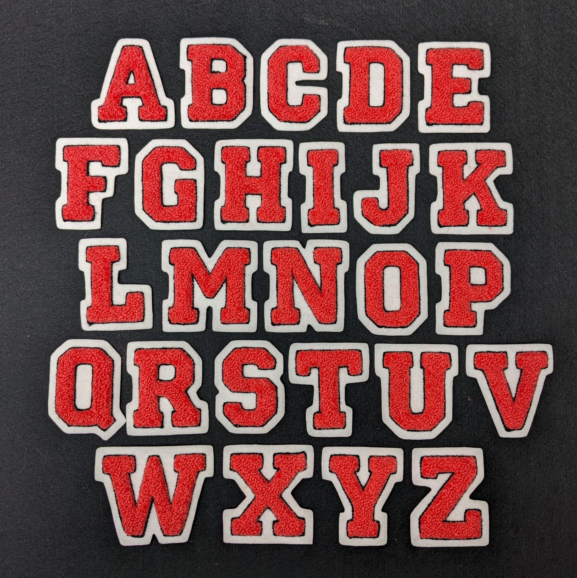 Coral chenille block letter with black outline on white colored felt.