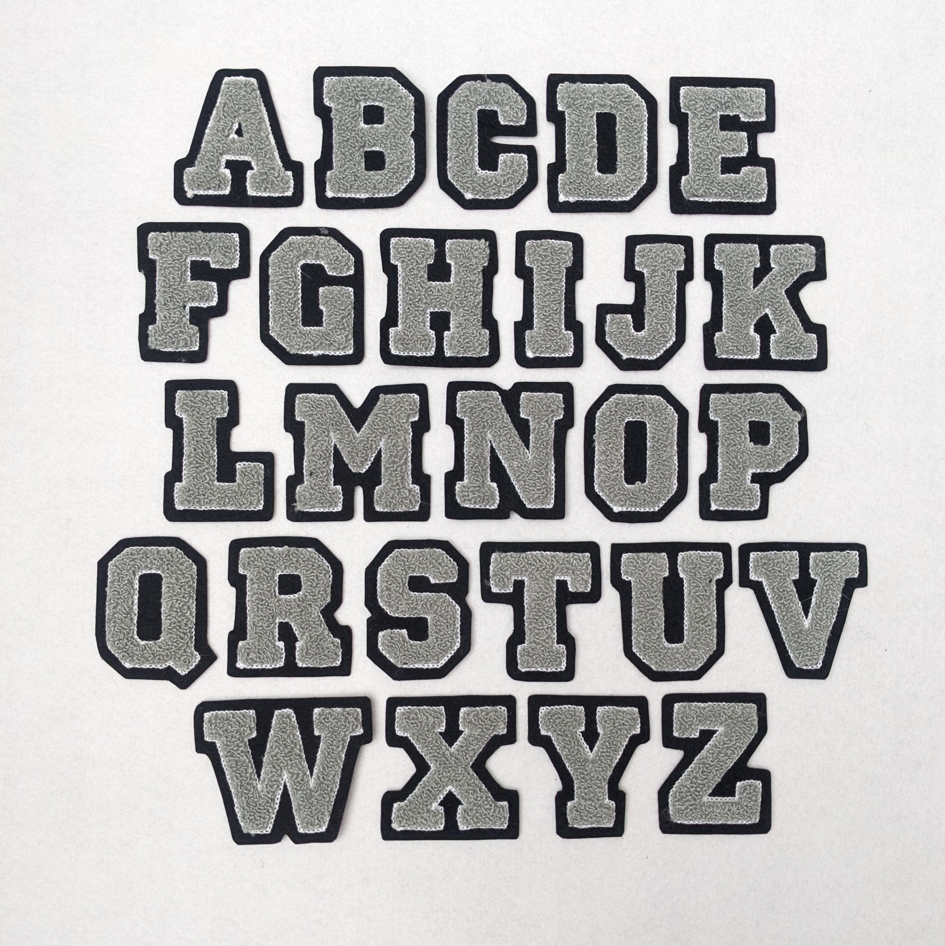 Grey chenille block letter with white outline on black colored felt.