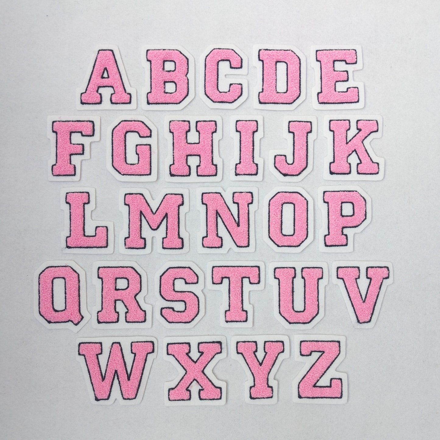 Pink chenille block letter with black outline on white colored felt.