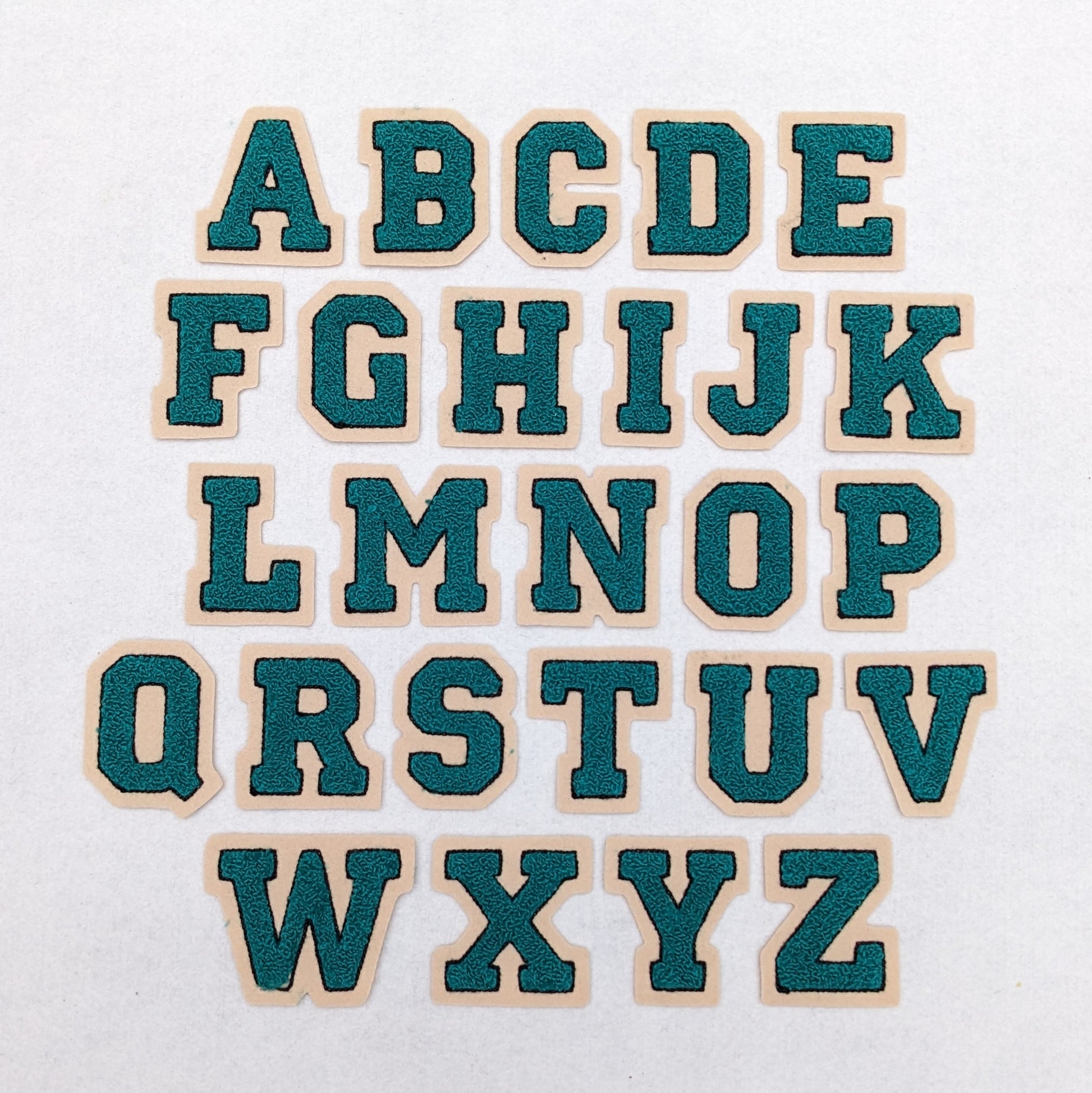 Teal chenille block letter with black outline on champagne colored felt.