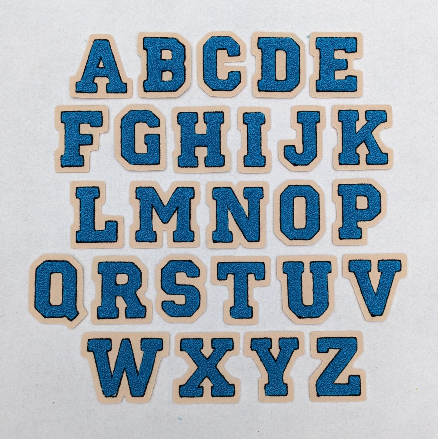 Turquoise chenille block letter with black outline on champagne colored felt.