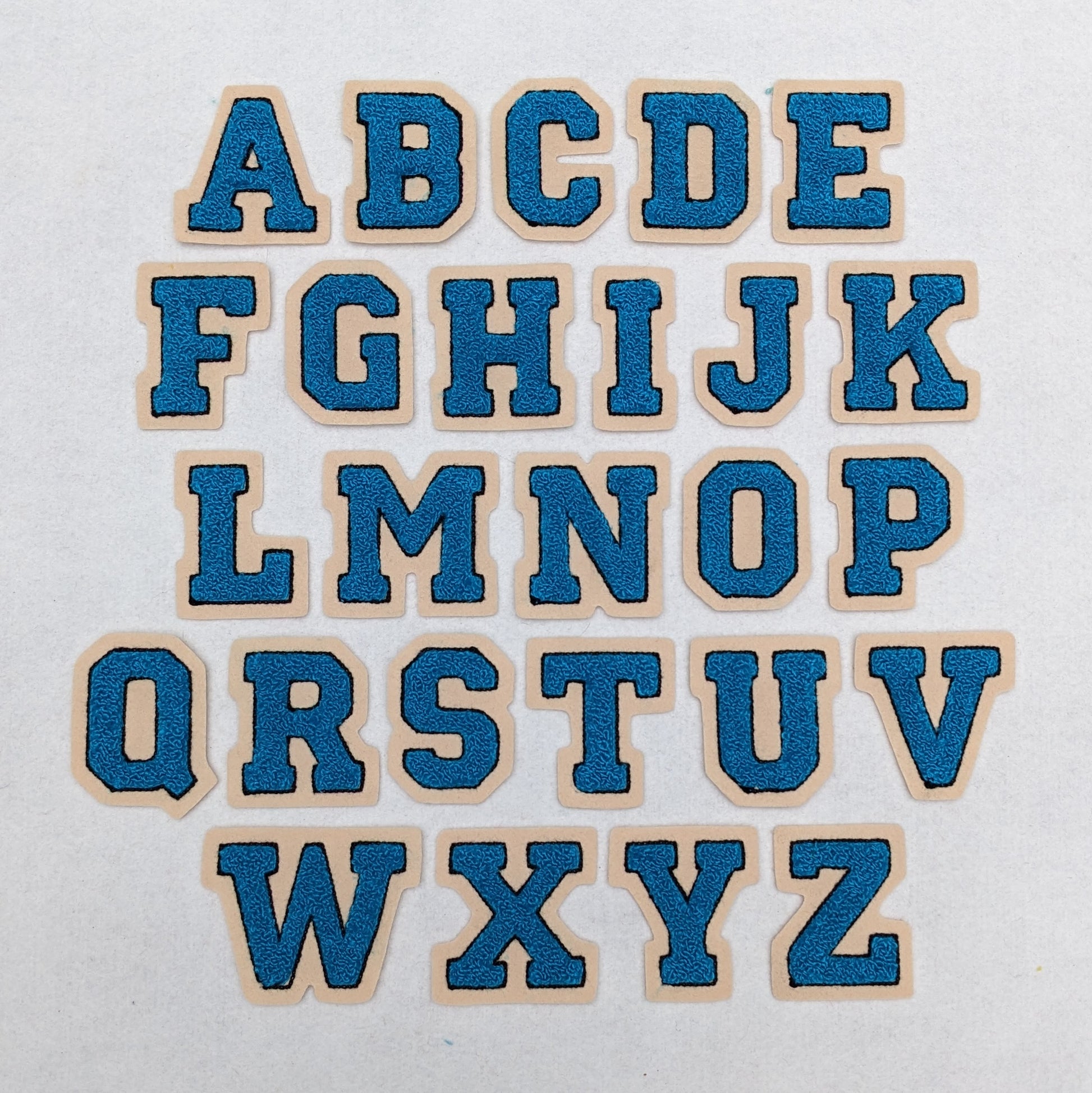 Turquoise chenille block letter with black outline on champagne colored felt.