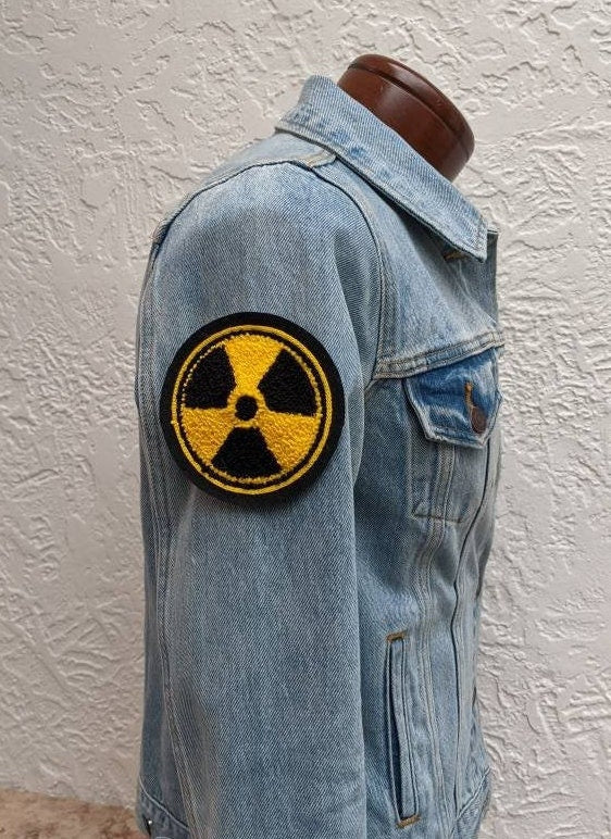 Denim jacket with a radiation symbol patch on a textured white background